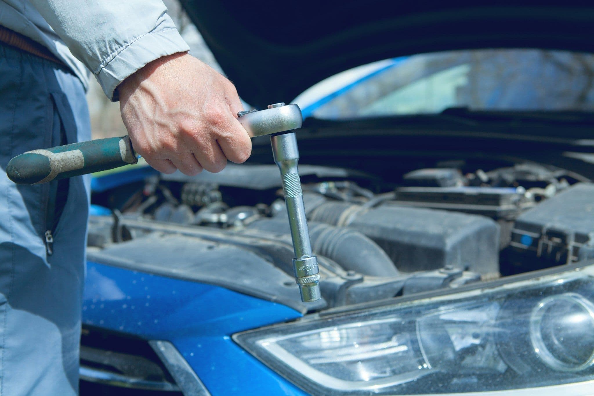 A mechanic works in a car’s engine compartment at a workshop.